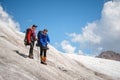 Two tourists, a man and a woman with backpacks and cats on their feet, stand on the ice in the background of the