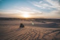 Two tourists ride on quad bike on sand dune on the background of a beautiful dawn with a bright sun early in the morning. Safari Royalty Free Stock Photo