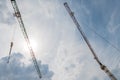 The two tower cranes and building construction site silhouette at cloudy blue and white sky and sun Royalty Free Stock Photo