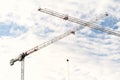 Two tower cranes with crossed booms at a construction site against a blue sky with white clouds