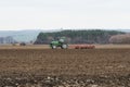 Two tractors plowing a field at a forest under a blue sky - Czech Republic