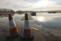 Two Traffic cones sit on a walkway preventing people going near a frozen lake