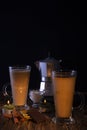 Two transparent glasses with latte, a coffee maker in the background on a wooden table with chocolate, anise, hazelnuts, lit by a Royalty Free Stock Photo