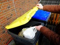 Two trash containers in the backyard of the private house for plastic and paper trash with a man throwing a trash bag in a yellow