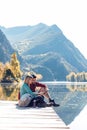 Two travel hikers using mobile phone while sitting in front of the lake in mountain