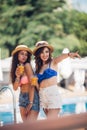 Two trendy cool hipster girls, friends, pretty brunette drink cocktails near the pool. Dressed in colorful swimsuit and shorts. Be