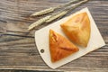 Two triangle traditional russian cabbage pies on a wooden cutting board laying on a wooden table, top view