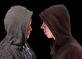 Two troubled teenage boys with black hoodie standing in front of each other in profile isolated on black background - stock Royalty Free Stock Photo