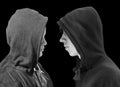 Two troubled teenage boys with black hoodie standing in front of each other in profile isolated on black background. Black and whi