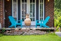 Two turquoise adirondack chairs and a chiminea on a crumbling brick porch in font of french doors on summer day with tiny American