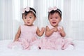Two twin babies in pink dress on bed, one looking, one crying Royalty Free Stock Photo
