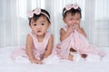 Two twin babies in pink dress on bed, one looking, one crying Royalty Free Stock Photo