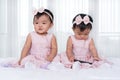 Two twin babies in pink dress on bed, one playing smart phone Royalty Free Stock Photo