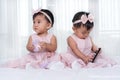 Two twin babies in pink dress on bed, one playing smart phone Royalty Free Stock Photo