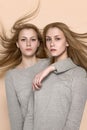 Two twin girls in a gray sweater posing in the studio on caramel pastel background