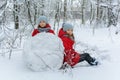 Two twin girls in red jackets rolling huge snowball to make snowman