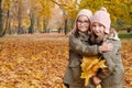 Two twin sisters pose for the camera with a bouquet of yellow leaves in the autumn park. Sisters hugging, smiling and Royalty Free Stock Photo