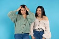 Two twin sisters in the same clothes surprised laugh at camera. Emotions on a blue background