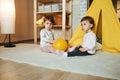 two twin sisters are sitting on the floor opposite each other playing with a yellow ball. Royalty Free Stock Photo