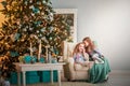 Two twin sisters sitting in a turquoise chair in the hall for the New Year. A sister whispers a secret in her ear in a decorat