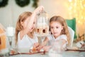 Twin sisters at a table in the kitchen playing with a ginger house for the New Year. The kitchen in bright colors is decorated Royalty Free Stock Photo