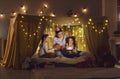 Two twin sisters with their mother are sitting in a cozy tent bed and celebrating their birthday.