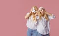 Two twin sleepless young women in pajamas and sleep masks on a pink background.