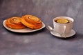 Two twisted cinnamon rolls on a plate and a cup of hot black tea with a slice of lemon on a gray background Royalty Free Stock Photo