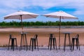 Two umbrellas with iron chair and table on stone floor.