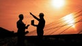 Two Unidentified Solar Power Engineers In Backlight At Sunset. Team of industrial colleagues using tablet monitoring Royalty Free Stock Photo