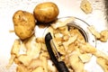 Two unpeeled potatoes lies in a wet kitchen sink next to potato skins and a black potato peeler Royalty Free Stock Photo