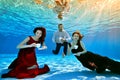 Two unusual cute girls and a guy pose and play underwater at the bottom of the pool with white cups in their hands, in