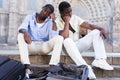 Two upset aframerican tourists sitting outdoors with empty bags