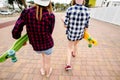 Two urban girls with longboards wearing checkered shirts going along the street in the city Royalty Free Stock Photo