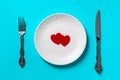 Two Valentine hearts on the white dinner plate, table knife and fork on a turquoise blue background. Concepts of heartbreaker,