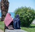 Two Veiled Muslim women in national dress are sitting on the promenade and looking on the beach . Concept of The life of