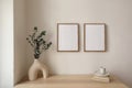 Two vertical picture frame mockup hanging on beige wall. Cup of coffee, books on wooden table. Vase with silver