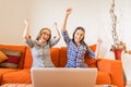 Two very happy girl cheering with hands up looking at laptop screen sitting at home sofa. Young winner women having success in Royalty Free Stock Photo
