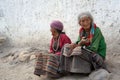 Two very old grandmother in traditional costumes sitting near the white wall on the street.