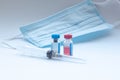 Two vials of the vaccine stand on a white background, behind the medical mask, in front of the syringe. The concept of