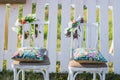 Two vintage white chairs, colorful velvet pillow and fence palisade on background decorated with flowers in boho style. Soft