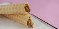 Two waffle cones with sweet boiled condensed milk in white plate on pastel pink background. Condensed tubules. Royalty Free Stock Photo