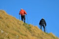 two with walking sticks ascending steep hill, clear day