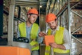 Two warehouse workers in helmets checking information online