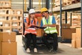 Two warehouse workers wearing safety hard hat and vest sitting on forklift truck in retail warehouse checking newly Royalty Free Stock Photo