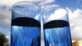 two water filled blue glasses with unique perspective and cloudy sky in background Royalty Free Stock Photo