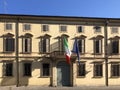 Two waving flags of Italy and EU. Building with windows and shutters across blue sky, old wooden door. Royalty Free Stock Photo