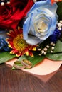 Two wedding rings against the background of a bridal bouquet from a blue rose and red colors Royalty Free Stock Photo