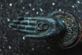 Two wedding rings on metal Buddha hand dark background. Spiritual love concept.