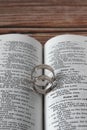 Two wedding rings on open Holy Bible Book placed on wooden background, vertical shot, a closeup